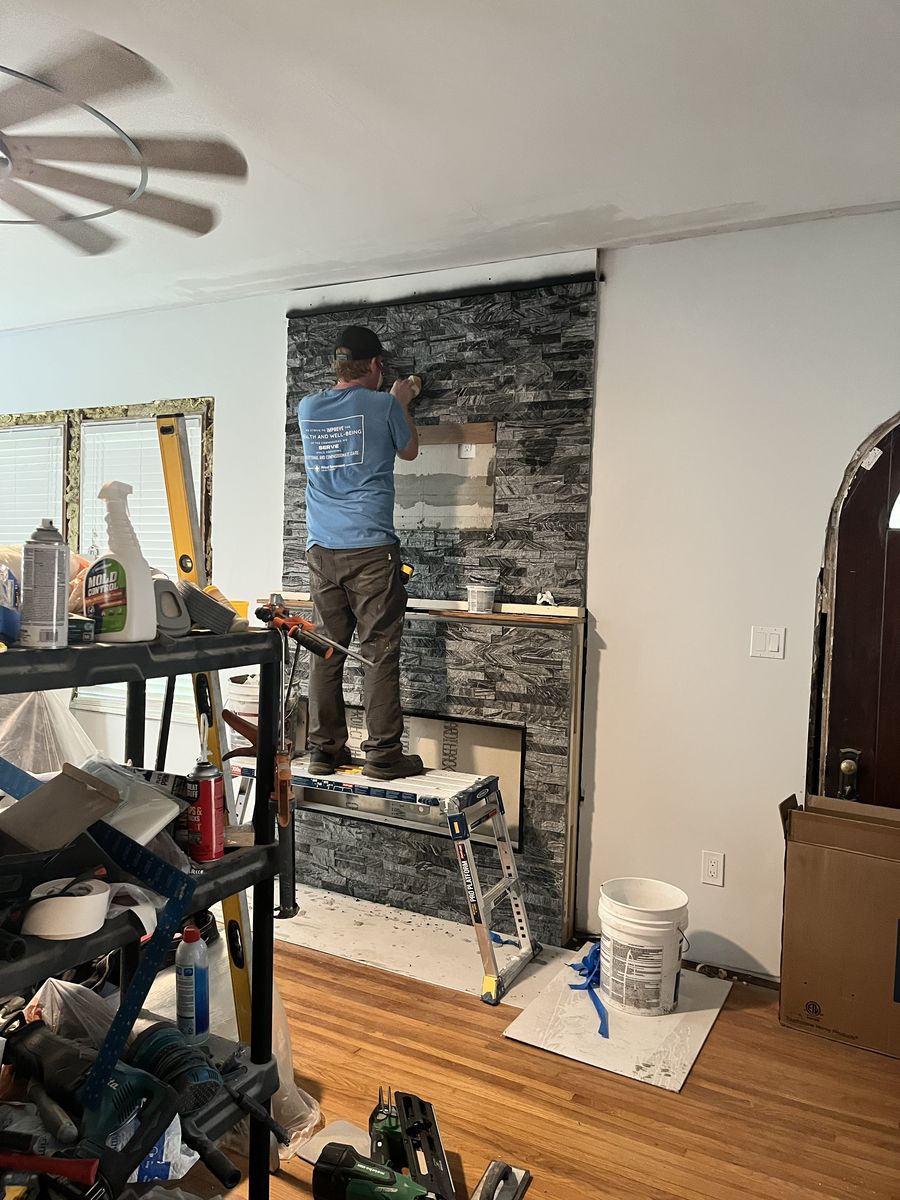 Richard Davis on a work platform installing stacked-stone tile on a fireplace wall