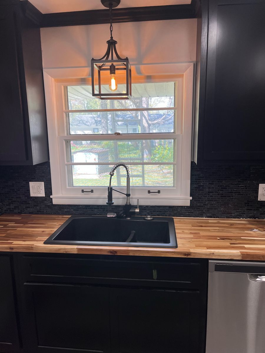 Kitchen with butcher-block counter, black sink and faucet, mosaic tile backsplash, and pendant light