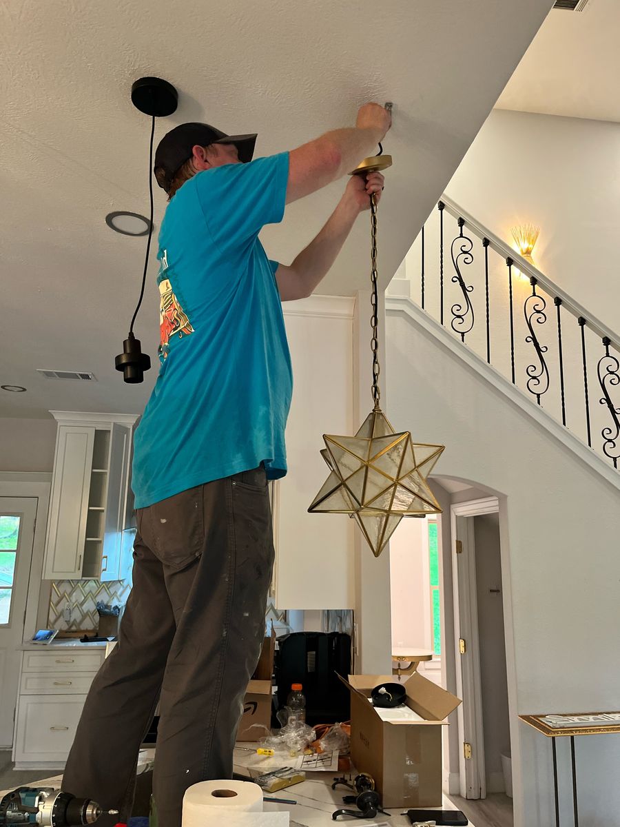 Richard on a ladder hanging a brass star pendant light in an entryway
